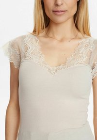 Top beige a righe con scollatura a V, caratterizzato da delicate maniche in pizzo e rifiniture, che mette in risalto intricati motivi floreali e una morbida texture.