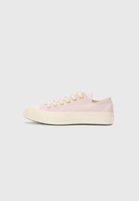 Light pink canvas sneakers with a flat design, featuring cream-colored rubber soles and gold eyelets, laced on the front.