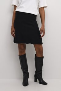 Crna pletena suknja s lepršavim oblikom, u kombinaciji s visokim crnim kožnim čizmama s šiljastim vrhom i blok petom. Jednostavna bijela majica.