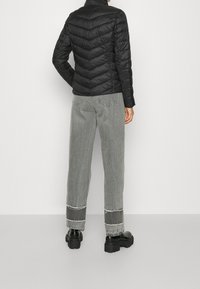 Černá péřová bunda s horizontálním prošíváním, doplněná světle šedými džíny s rovnými nohavicemi, které mají ošuntělý lem, a robustními černými botami.