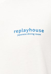 Λευκό ύφασμα με μπλε κείμενο "replayhouse" πάνω από μικρότερο κείμενο "japanese dining room" κεντραρισμένο στην επιφάνεια.