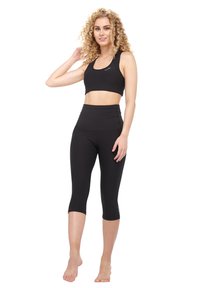 Top corto atlético negro con tirantes finos, combinado con leggings capri negros de cintura alta. Tela suave y elástica sin patrones visibles.