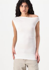 Haut blanc à épaules dénudées en tissu léger avec une silhouette ajustée. Présente des manches courtes et une texture lisse, légèrement transparente.
