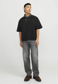 Svart oversized t-shirt med korta ärmar, matchad med ljusgrå raka jeans. En svart bandana är knuten runt halsen.