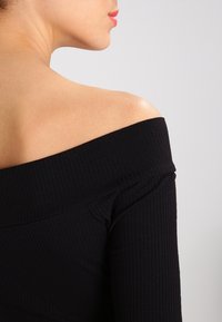 Schwarzes Off-Shoulder-Oberteil mit gerippter Textur, taillierter Passform und langen Ärmeln. Enthüllt das Schlüsselbein und die oberen Schultern.