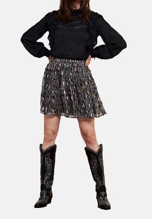 Zwarte blouse met ruches, doorschijnend paneel. Meerkleurige geplooide rok, tot op de knie. Zwarte cowboylaarzen met decoratieve borduurwerk.