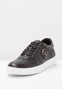 Sneaker nera a basso profilo con motivo a logo trapuntato, emblema tondo in metallo sul lato, colletto borchiato, stringhe nere e suola bianca.