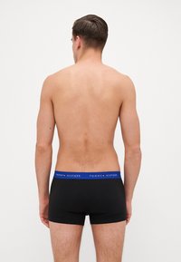 Fekete boxer alsónadrág kék derékpánttal, amelyen a "Tommy Hilfiger" logó látható; sima anyag, szoros illeszkedés és combközép hosszúság.