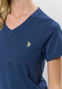 Tengerészkék pamut póló V nyakkivágással. Bal mellrészen egy kis arany logóval rendelkezik. Rövid ujjú, sima tapintású és enyhén fit.