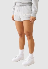 Szare bawełniane szorty ze sznurkiem w pasie, z haftowanym logo po lewej stronie, zestawione z białymi sneakersami i skarpetkami.
