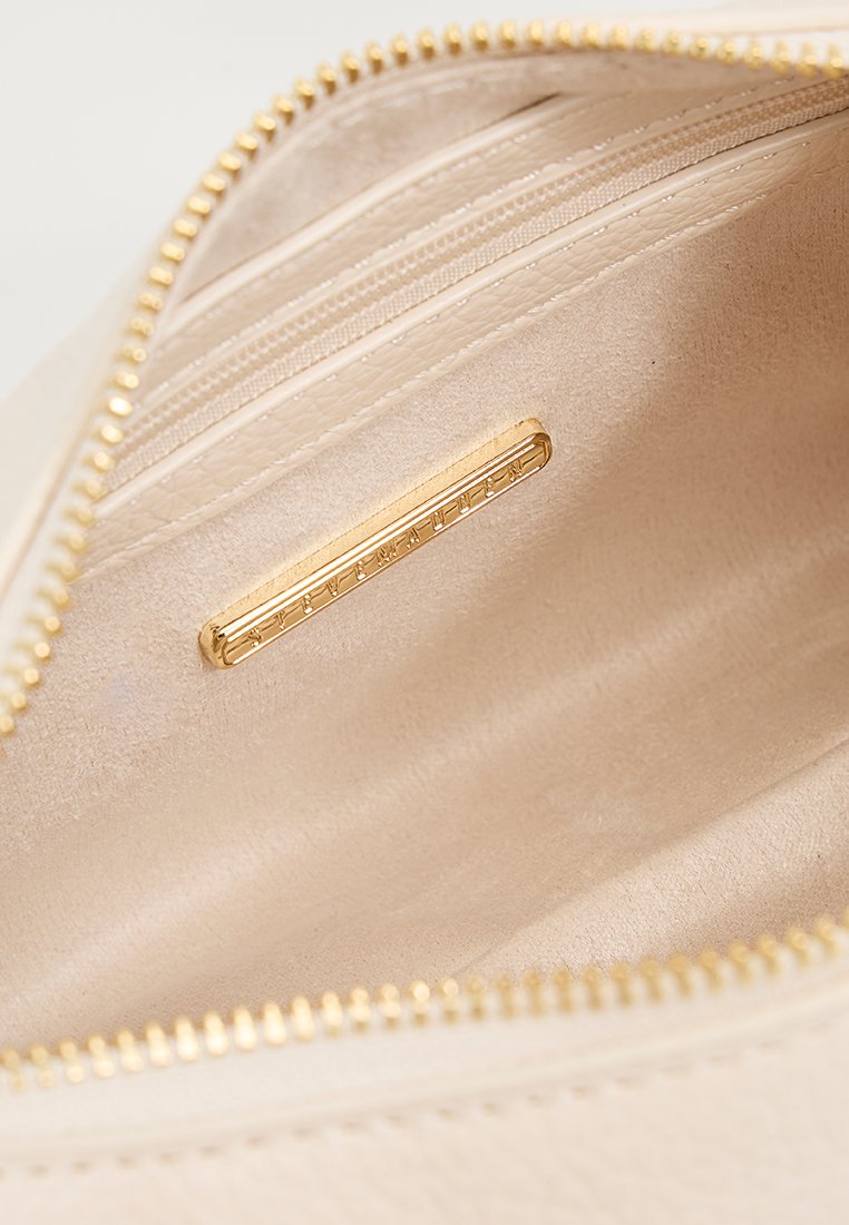 Interno di una borsa in pelle beige con una texture liscia, dotato di una cerniera in tonalità dorate, di più slot per carte e di una piastrina per il brand dorata.