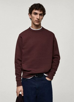 Tricou burgund cu guler rotund și mâneci lungi, purtat cu un tricou alb pe dedesubt, asortat cu blugi din denim închis.