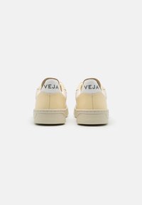 Sneakers beige chiaro con una finitura testurizzata, caratterizzati da un accento bianco nel tallone e un audace branding "VEJA" sul retro. Suola in gomma liscia.