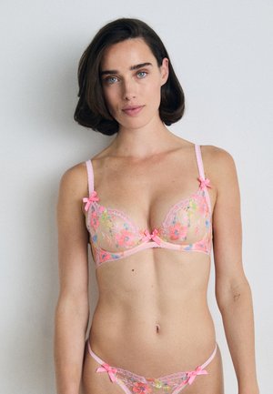 Kanten lingerieset in een doorzichtige bloemmotief, met roze accenten en strikjes, voorzien van verstelbare banden en een delicate golvende afwerking.