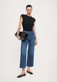Top negro de manga corta, jeans de pierna ancha de lavado medio, sosteniendo un clutch de cuero negro, combinado con zapatos planos negros. Líneas limpias y estilo minimalista.