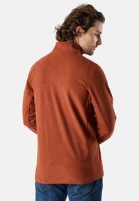 Pullover in fleece arancio bruciato con colletto alto, dotato di una texture liscia e dettagli sullo yoke posteriore, indossato con jeans blu.