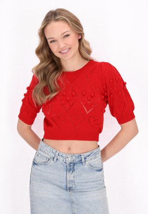 Piros kötött crop top rövid puffujjakkal, szív alakú kivágásokkal és texturált pom-pomokkal, világos farmer szoknyával párosítva.