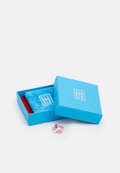 Inel metalic roz cu un design ondulat, având o piatră prețioasă purpurie, lângă două cutii din carton bleu cu un insert din catifea și logo.