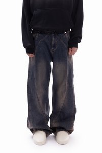 Wide-leg denim jeans in dark blue with lighter faded patches. Features curved seams and a loose fit, styled with a black hoodie.