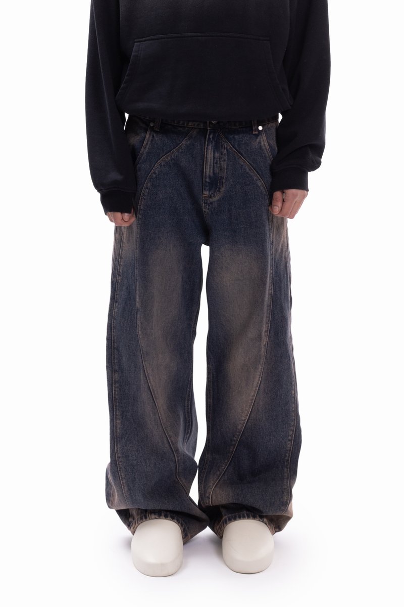 Wide-leg denim jeans in dark blue with lighter faded patches. Features curved seams and a loose fit, styled with a black hoodie.