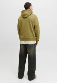 Oliwkowy hoodie z dużą tylną kieszenią i kapturem na sznurku, w połączeniu z szerokimi ciemnymi dżinsami z wyblakłą fakturą.
