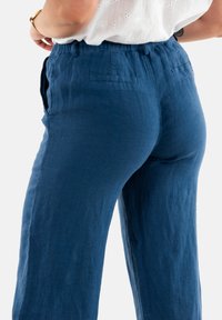Pantalones de lino azules con una cinturilla elástica, bolsillos laterales y bolsillos traseros; tejido ligero con un acabado ligeramente texturizado.