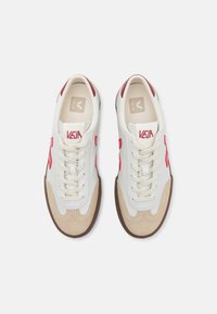 Zapatillas blancas de cuero con acentos rojos y detalles en ante beige. Presentan un diseño de cordones, punta redondeada y suela de goma marrón.
