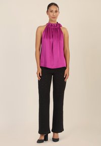 Top halter en fucsia con escote fruncido, combinado con pantalones negros que presentan pequeños acentos decorativos. Silueta simple y elegante; textura suave.