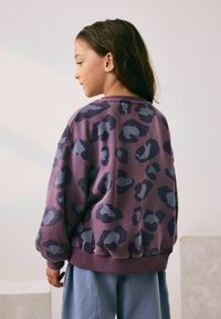 Lilla sweatshirt med leopardprint i mørkeblå, med ribstrikkede manchetter og kant, parret med lyseblå bukser. Glat tekstur.