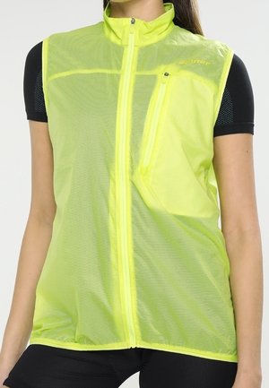 Vrouw draagt een mouwloos neongeel meshvest met een ritssluiting aan de voorkant en een borstzak met rits over een zwart topje met korte mouwen.