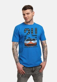 Camiseta de algodón azul con un estampado gráfico de un coche de carreras y texto, con estrellas en blanco y negro arriba y acentos rojos en el coche.