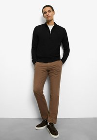 Schwarzer Zip-Hals Pullover, braune Chinos und dunkelbraune Wildleder-Sneaker. Einfaches Design, figurbetonte Form, glatte Textur. Klarer Farbkontrast.