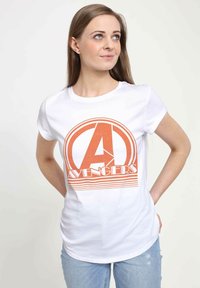 Biała bawełniana koszulka z krótkim rękawem, z pomarańczowym nadrukiem logo "Avengers" z okrągłymi akcentami i poziomymi liniami. Luźny krój.