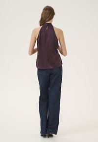 Donkerpaarse satijnen haltertop met een sleutelgat achterkant, gecombineerd met hoog-gewijde blauwe denim jeans en zwarte hakken, met een losse pasvorm.