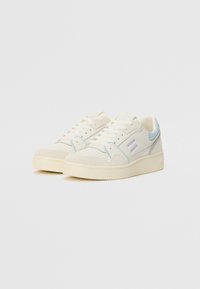Low-top sneakers with a cream leather upper, light blue accents, perforated toe box, flat white laces, and a textured rubber sole.