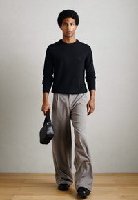 Cămașă neagră cu mânecă lungă, pantaloni gri cu picioare late, geantă texturată neagră și pantofi negri. Design simplu pe un fundal neutru.