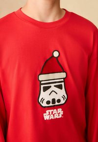 Červená mikina má na sobě grafiku Stormtroopera s vánoční čepicí, s černými obrysy a bílým nápisem "STAR WARS" níže.