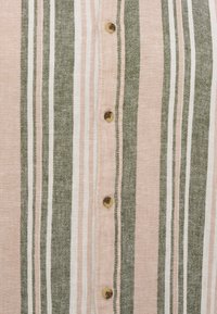 Κάθετες ρίγες σε πράσινο, ροζ και λευκό πάνω σε ύφασμα με μια κεντρική σειρά από τέσσερα καφέ κουμπιά ραμμένα σε ροζ πατιλέτα.