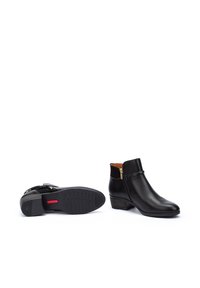 Botines de cuero negro hasta el tobillo con textura suave, punta redondeada y un tacón pequeño. Cuentan con una cremallera lateral y un acento rojo en la suela.