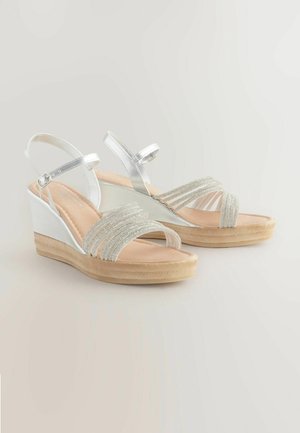 Peskasta obutev z wedge peto z srebrnimi metalnimi trakovi in perlicami, z bež notranjostjo in teksturirano gumijasto podplatom.