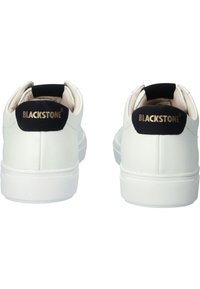 Sneakers in pelle bianca con un design semplice, suola piatta bianca e dettagli neri sul tallone con la scritta "BLACKSTONE" in lettere dorate.