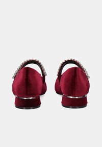 Zapatos de terciopelo burdeos con tacón bajo, que presentan un acento de gema brillante en la correa trasera. Textura suave y diseño de punta redondeada.