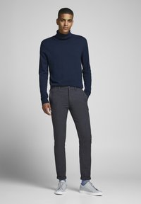 Navy turtleneck sweater parret med strukturerede mørkegrå bukser og lysegrå sneakers, med minimalistisk design og skræddersyet pasform.