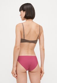Reggiseno marrone con spalline regolabili e chiusura a gancio, abbinato a slip rosa uniforme. Tessuto liscio con un design semplice e senza cuciture.