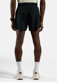 Schwarze Sportshorts mit einem elastischen Bund, die bis zur Mitte des Oberschenkels reichen, kombiniert mit weißen Kniestrümpfen und hellen Sneakern.