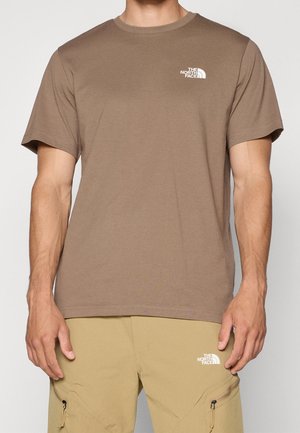 Homme portant un t-shirt marron The North Face et un short cargo beige, tous deux avec des logos de marque blancs à l'avant.