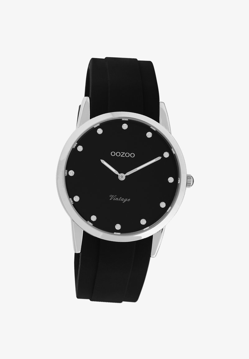 Montre avec bracelet en silicone noir, cadran noir, accents argentés et index des heures en cristal. Elle présente un design minimaliste et un boîtier en métal.