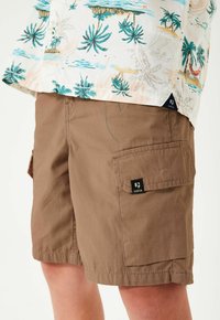 Bruine cargoshorts met meerdere zakken, gemaakt van lichte stof. Heeft een patchlogo aan de zijkant en zichtbare stikseldetails.