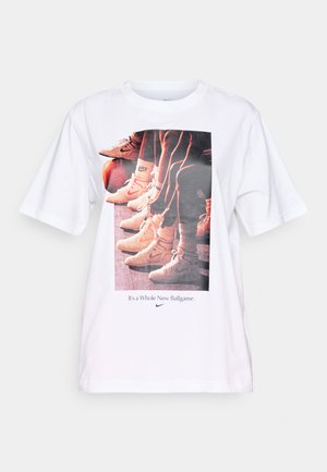 T-shirt blanc avec un imprimé graphique de chaussures de basketball et le texte "C'est un tout nouveau jeu" en bleu, col rond, manches courtes.