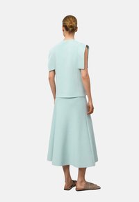 Jasno miętowy dwuczęściowy zestaw składający się z dopasowanej bluzki z krótkimi rękawami oraz rozkloszowanej spódnicy midi, wykonany z gładkiego, teksturowanego materiału.